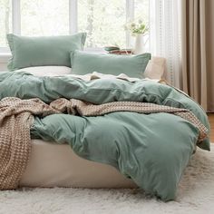 an unmade bed in front of a window with green sheets and blankets on it