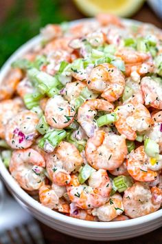 a bowl filled with shrimp and celery on top of a table next to a fork