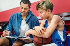 a man sitting next to a little boy on a basketball court while holding a clipboard