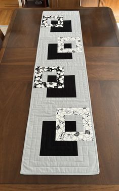 a table runner with black and white quilts on it, sitting on top of a wooden table