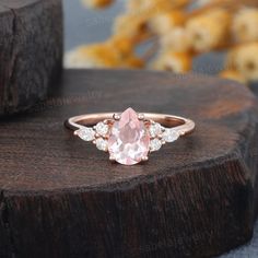 an oval shaped pink sapphire and diamond ring on top of a wooden stand with flowers in the background