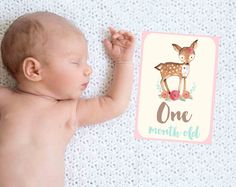 a baby laying on top of a white blanket next to a one month old book