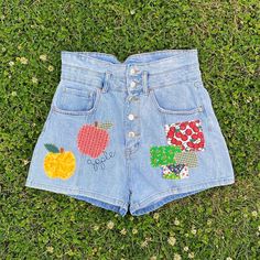 a pair of jean shorts with applique apples and flowers on them sitting in the grass