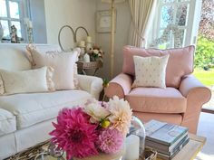 a living room filled with furniture and flowers on top of a coffee table in front of a window