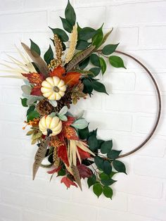 a wreath with pumpkins, leaves and other decorations hanging on a wall in front of a brick wall