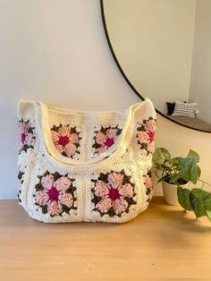 a crocheted purse sitting on top of a wooden table next to a potted plant