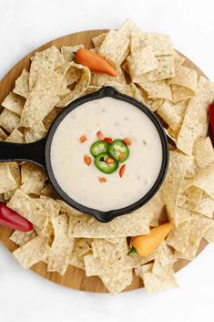 a plate with chips and dip on it next to some chili peppers, carrots and jalapenos