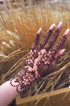 a woman's hand with henna on it in front of some tall grass