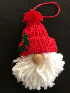 a red and white knitted santa claus ornament on a black table top