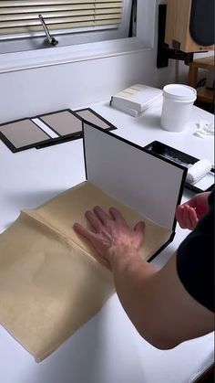 a person holding their hand out in an open box on top of a table next to a window