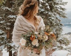 a woman standing in the snow holding a bridal bouquet and looking off into the distance