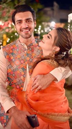 a man and woman standing next to each other in front of a christmas tree with lights