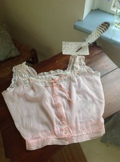 a cotton and lace camisole in a pink color with coral pink silk ribbon, and beautiful buttons. there is a little faded stain at the front ( photo 7.) in excellent condition bust 88 cm  34.5" waist 63 cm 24 3/4" Fitted Pink Camisole With Lace Top, Pink Fitted Lace Top Camisole, Fitted Lace Top Pink Camisole, Fitted Pink Top With Delicate Lace, Fitted Pink Delicate Lace Top, Pink Lace Trim Camisole In Coquette Style, Pink Lace Trim Coquette Camisole, Pink Summer Camisole With Delicate Lace, Pink Lace Top Camisole