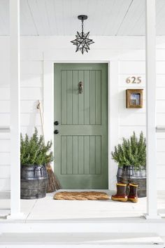 a green front door on a white house with two buckets full of potted plants