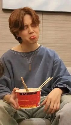 a woman sitting on a couch holding a cup with chopsticks in it