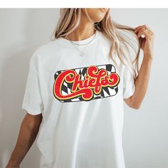 You will love this super cute and cozy Kansas City Chiefs shirt! This is a unisex fit t-shirt, made with direct to film transfer, no vinyl or sublimation is used.  T-shirts are comfort colors soft washed garment-dyed tees, renowned for their softness, comfort, and durability. Made with 100% ring-spun cotton, and sure to make an excellent choice for comfortable daily wear. T-shirts have double needle stitching throughout, sewn in twill label, and ribbed collar.  In order to provide the most color choices, sweatshirts in Pepper and Ivory are made using Comfort Colors 100% soft ring-spun cotton, while sweatshirts in white, black, grey, red, and sand are made using Gildan Cozy Feel, 50% cotton 50% poly blend. Both have a ribbed collar and relaxed fit and will make a great addition to your game Kc Chiefs Shirts Vinyl, Trendy Crew Neck Sublimation T-shirt With Screen Print, Pop Culture Relaxed Fit Shirt With Letter Print, White Pop Culture Shirt With Letter Print, Funny Print Graphic Tee, Trendy Short Sleeve Sublimation T-shirt With Graphic Print, Trendy T-shirt With Funny Print For Fans, Pop Culture Short Sleeve Shirt With Letter Print, Trendy Sublimation Short Sleeve Graphic Print