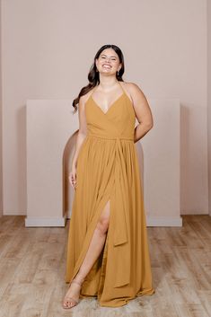 a woman in a tan dress standing on a wooden floor with her arms behind her back