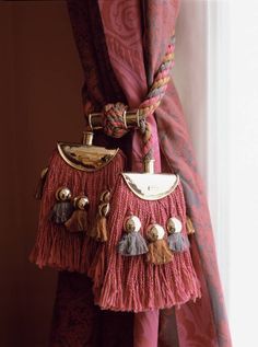 a purse hanging on the side of a curtain with tassels attached to it