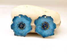 two blue flower shaped earrings sitting on top of a white rock next to each other