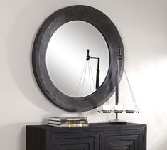 a round mirror hanging on the wall above a black cabinet with books and a lamp