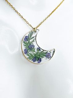 Embrace the enchanting allure of our Lavender Moon necklace. This celestial beauty features a delicate crescent moon pendant adorned with real dried purple flowers and green foliage, preserved in crystal-clear resin with a touch of gold paint trimming. The soft purple hues of the lavender color petals reflect the tranquility of a moonlit garden. Suspended on a 14k gold plated stainless steel chain, this necklace exudes a sense of elegance and serenity. With each gentle sway, the Lavender Moon pendant captures the essence of celestial magic. Adorn yourself with this piece of nature's wonder and let the Lavender Moon illuminate your every step. Unveil the enchantment of Lavender Moon. Shop now and add a touch of celestial beauty to your jewelry collection. NOTE TO BUYER: All jewelry is made Nature-inspired Round Pendant Jewelry With Moon Charm, Nature-inspired Moon Charm Pendant Necklace, Nature-inspired Moon Charm Necklace As Gift, Nature-inspired Moon Charm Necklace As A Gift, Nature-inspired Moon Charm Jewelry As A Gift, Nature-inspired Moon Charm Necklace For Gift, Nature-inspired Necklace With Moon Charm Round Pendant, Nature-inspired Necklace With Round Moon Charm Pendant, Nature-inspired Round Pendant Necklace With Moon Charm