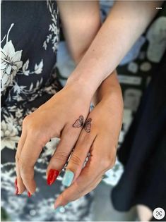 two hands holding each other with tattoos on their fingers and one has a butterfly tattoo on it