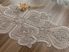 an intricately designed table runner on a wooden floor with dried flowers in the background