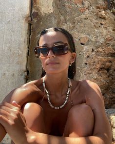 a woman with no shirt on posing for the camera in front of a stone wall