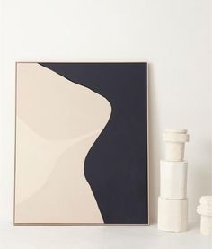 a white vase sitting on top of a table next to a black and white painting