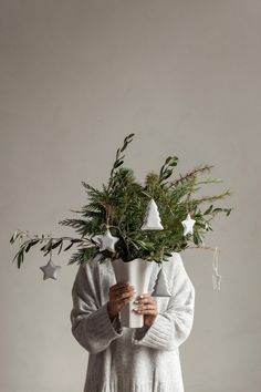 a person holding a cup with plants on top of their head and wearing a sweater