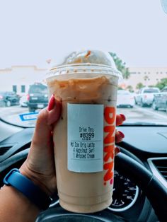 a woman holding up a cup of coffee in her hand while driving down the street