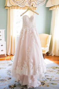 a wedding dress hanging on a hanger in front of a window with drapes