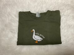 Silly Goose Comfort Colors Shirt, Embroidered Goose Crewneck T-Shirt, Silly Goose Shirt, Embroidered Comfort Colors Shirt, Funny Goose Shirt This embroidered silly goose shirt is everything. Perfect to tell everyone you're a silly goose!   These are embroidered comfort colors shirts they are so comfy and we use high quality thread on all our embroidery items.  ✨ 100% Cotton ✨ Pre-shrunk ✨ Relaxed fit Care: Machine wash: warm  Tumble dry: low Do not iron directly on the print Please message me if Fall Embroidered Crew Neck Shirt, Embroidered Crew Neck Shirt For Fall, Casual Long Sleeve Shirt With Custom Embroidery, Green Long Sleeve T-shirt With Custom Embroidery, Casual Embroidered Long Sleeve T-shirt, Casual Long Sleeve Embroidered T-shirt, Green Embroidered Long Sleeve T-shirt, Casual Crew Neck Shirt With Machine Embroidery, Casual Cotton Shirt With Machine Embroidery