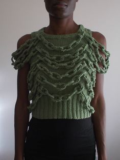 a woman wearing a green knitted top with ruffles on the shoulders and sides