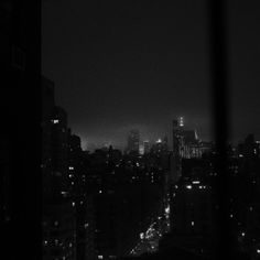 the city skyline is lit up at night in black and white, as seen through a window