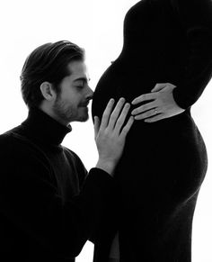 a black and white photo of a man kissing a pregnant woman's belly with her hands