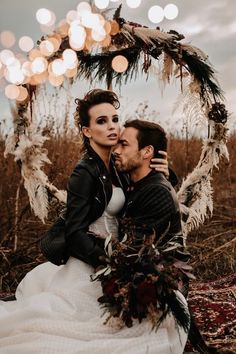 a man and woman sitting in front of a wreath with lights on the ground behind them