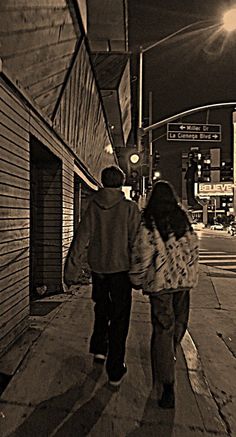 a man and woman walking down the sidewalk in front of an empty building at night