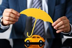 a man in a suit holding an umbrella over a toy car that is on top of a table