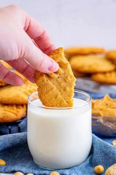 a hand dipping a cracker into a glass of milk with cookies in the background