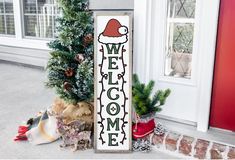 a welcome sign sitting on the side of a building next to a christmas tree and potted plants