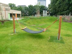 an empty hammock in the middle of a grassy area with trees and buildings in the background