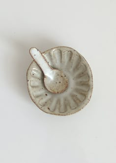 a small white dish with a spoon in it's center on a white surface