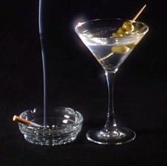 two martini glasses with olives in them on a black background, one has a stick sticking out of it