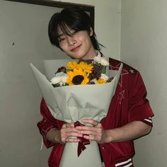 a woman holding a bouquet of sunflowers in her hands while standing next to a wall