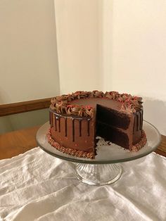 a chocolate cake sitting on top of a glass platter next to a white table cloth