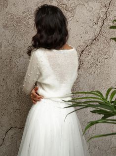 a woman in a white dress standing next to a wall and looking at the ground