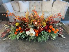 an arrangement of flowers and greenery sits on the floor in front of a couch