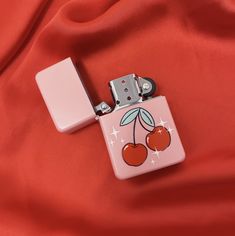 a pink lighter with cherries on it sitting on a red cloth next to another lighter