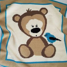 a crocheted teddy bear with a blue bird on it's back, sitting next to a brown and white blanket